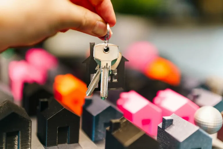 A hand holding house keys over miniature houses